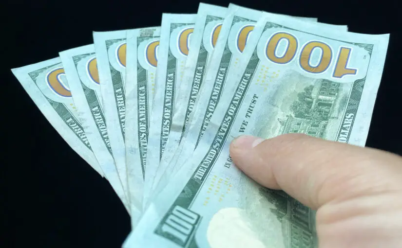 Photo of $100 bills held in person's hand.