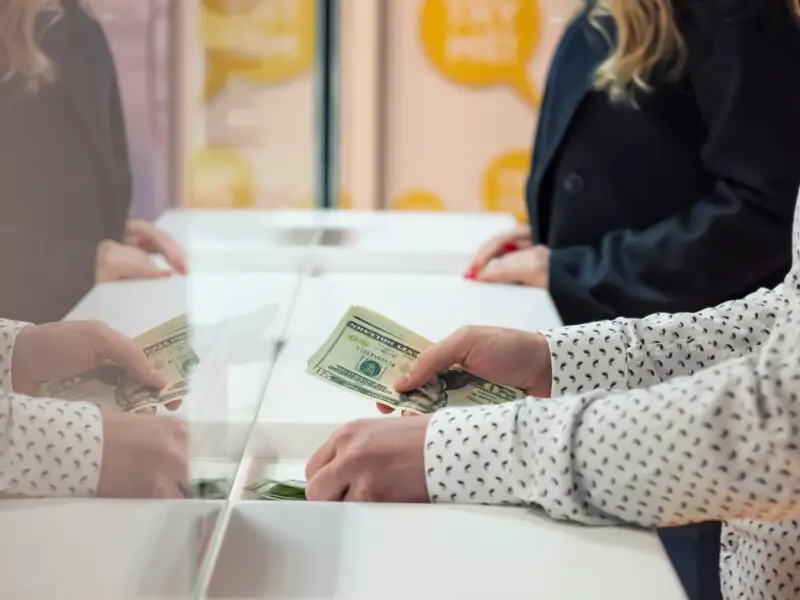 Person exchanges cash with a teller inside a bank.