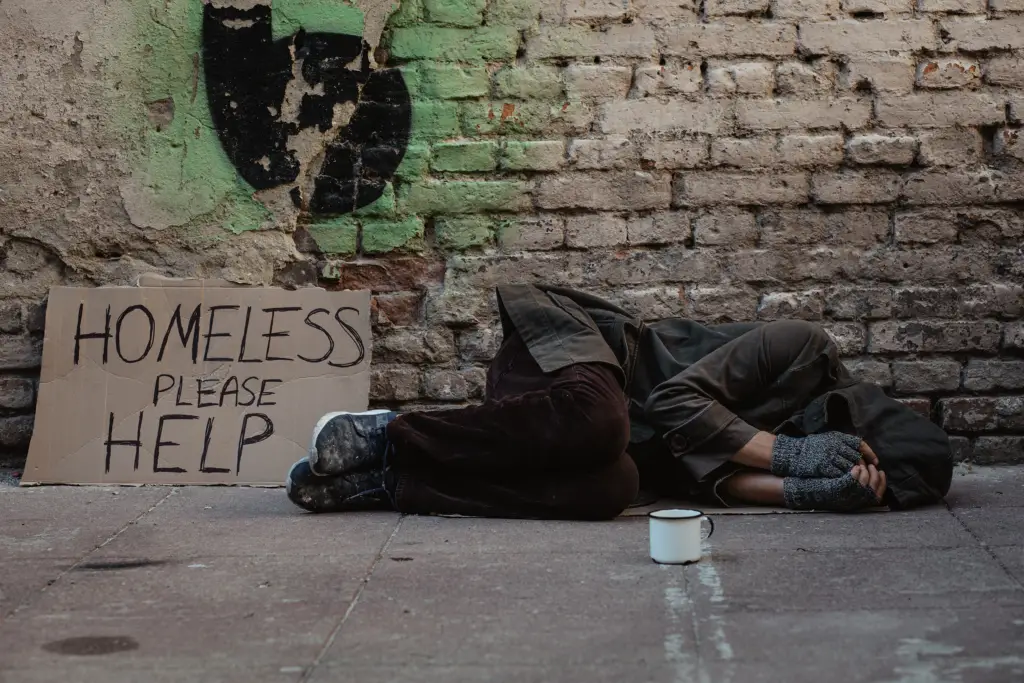 Photo of homeless man lies on the street in the shadow of the old building