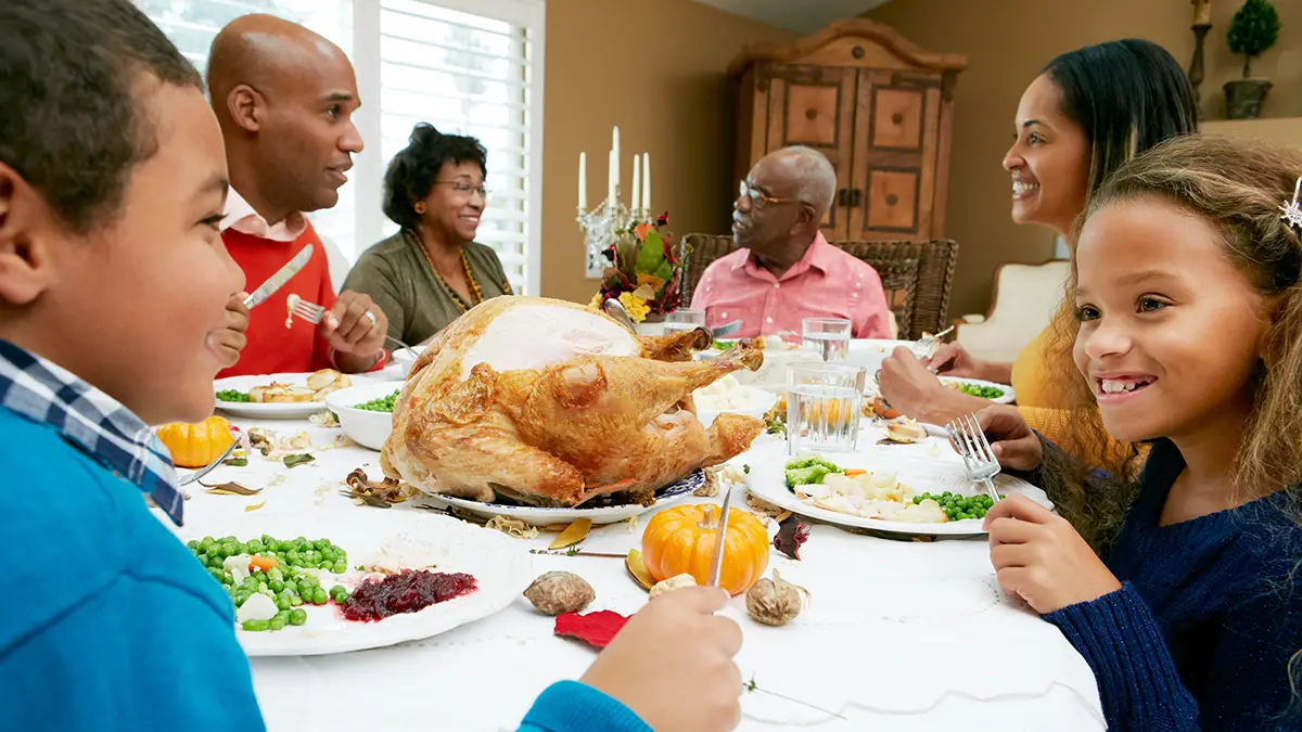 Photo of multi-generational family talking over Thanksgiving dinner - Photo by Adobe Stock