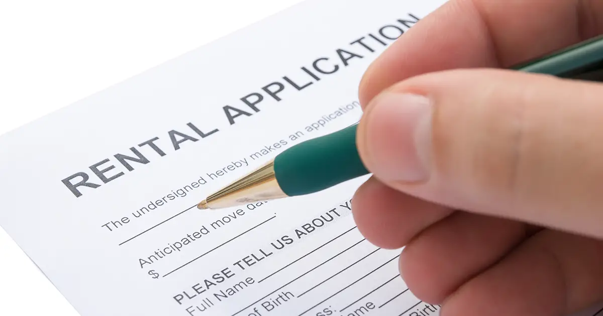 Close up photo of a paper rental application being filled out by a person using a pen. Photo by Adobe Stock.
